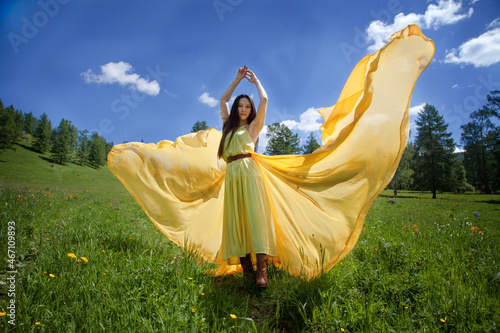 A beautiful Altai girl in a yellow dress walks in the Altai mountains in the summer. Tourism concept.