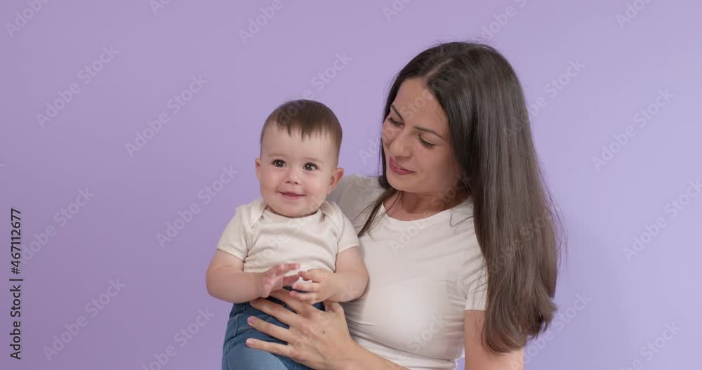Good-looking brunette woman mother holding toddler girl child in hands, enjoy motherood, happy childhood, woman teach and talk with child, kid is learning environment. isolated purple background Good-looking brunette woman mother holding toddler girl child in hands, enjoy motherood, happy childhood, woman teach and talk with child, kid is learning environment. isolated purple background