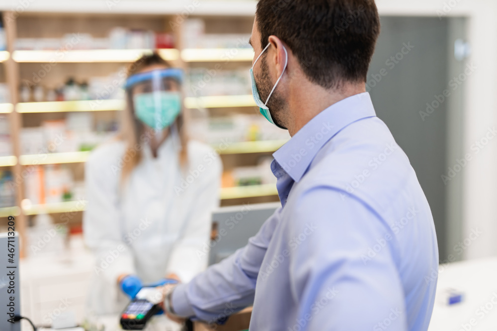 Male customer with protective mask on his face buying pills in modern drugstore.