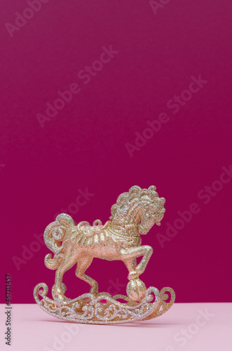 Golden and silver Christmas toy horse decoration on a pastel pink and dark mauve background. Copy space.