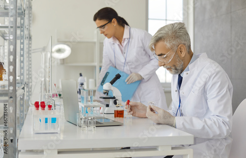 Senior male scientist doing experiments in laboratory by pipetting samples of cell culture medium. Medical  pharmaceutical and scientific research and development concept. Side view.