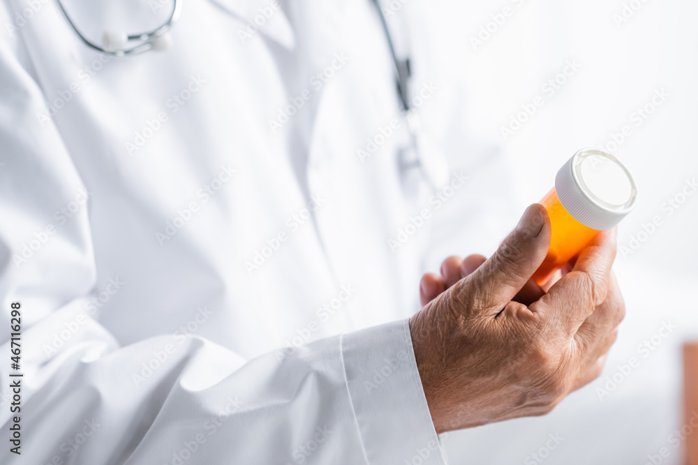Cropped view of senior doctor holding jar with pills in hospital Cropped view of senior doctor holding jar with pills in hospital