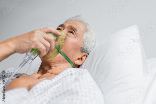 Elderly asian patient breathing in oxygen mask on bed in clinic