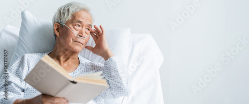 Elderly asian patient with nasal cannula holding book on hospital bed, banner