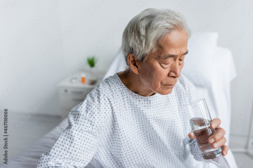 Elderly asian patient holding glass of water in hospital ward Elderly asian patient holding glass of water in hospital ward