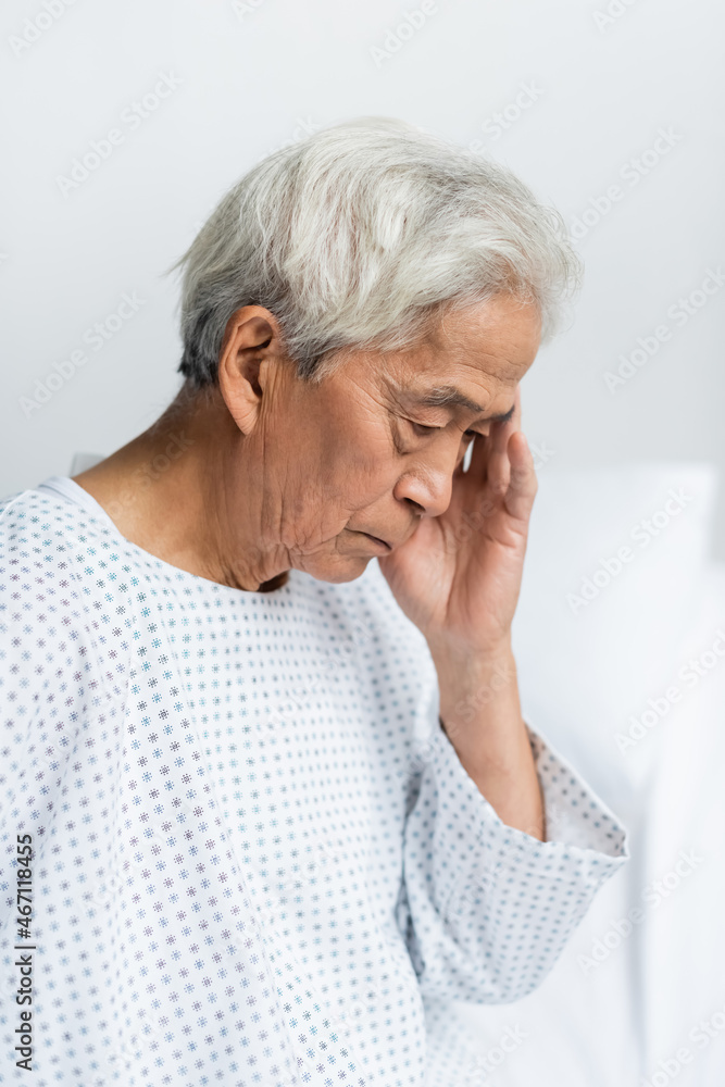 Upset senior asian patient in gown in hospital ward Upset senior asian patient in gown in hospital ward