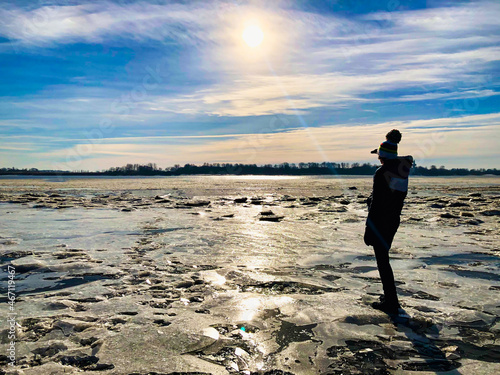 Silhouette of child looking far away with hand over head on icy shore of the river elbe in Hamburg, Germany . Searching concept. Ice and Snow, Sunny sky, reflection.