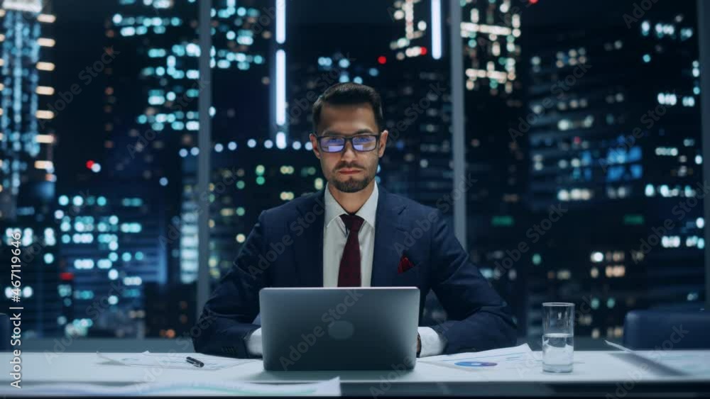 Portrait of a Successful Handsome Businessman Working on Laptop Computer in Big City Office Late in the Evening. Happy Competent Manager in Stylish Dark Blue Suit Smiles and Poses for Camera. Portrait of a Successful Handsome Businessman Working on Laptop Computer in Big City Office Late in the Evening. Happy Competent Manager in Stylish Dark Blue Suit Smiles and Poses for Camera.