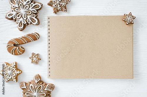 Christmas gingerbread and brown notebook on white wooden table.