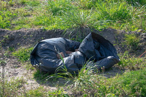 Garbage bag dumped in the grass of a meadow and weighted with bricks