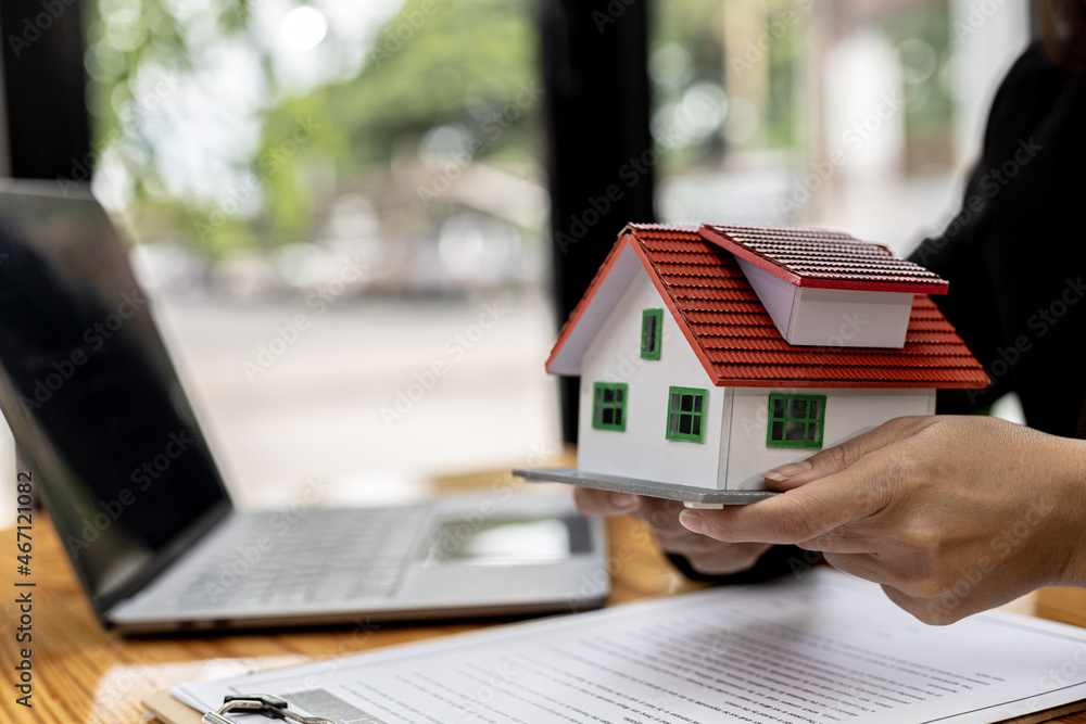Fototapeta premium Model of a house placed on a woman's hand, a housing salesman in the project, a portrait holding a house project to the front similar to delivering homes to customers. Real estate trading ideas.