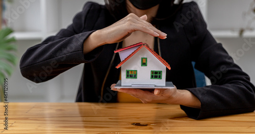 Woman puts her hand on top of a miniature house model, photo of home insurance concept, when buying a new home should have home insurance to be sure if there is any danger to the home.