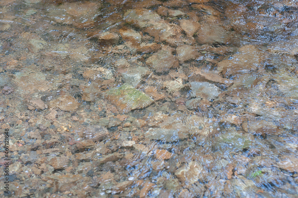 Sun glare on surface water and smooth stones at bottom stream, background. Transparent water in river with rocky bottom, fast flow Sun glare on surface water and smooth stones at bottom stream, background. Transparent water in river with rocky bottom, fast flow
