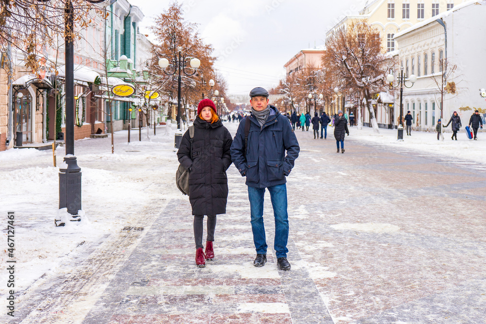 Tourists man and woman walking along city street in winter cloudy day. People spending winter weekend in city. Father and daughter wearing winter casual clothes. Urban vacation concept Tourists man and woman walking along city street in winter cloudy day. People spending winter weekend in city. Father and daughter wearing winter casual clothes. Urban vacation concept
