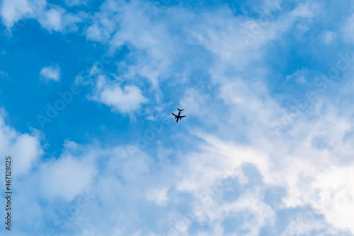Dark silhouette of a flying passenger plane against a blue sky with clouds
