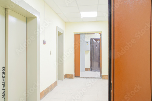 An empty, light corridor with doors in a new, almost completed, apartment building. A door in a protective foil at the last stage of construction.