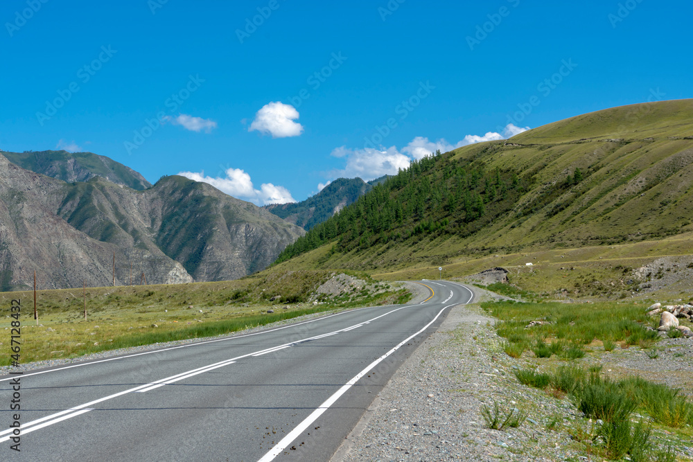 peaks of mountains against the sky with white clouds. Summer sunny day. Mountain asphalt road
