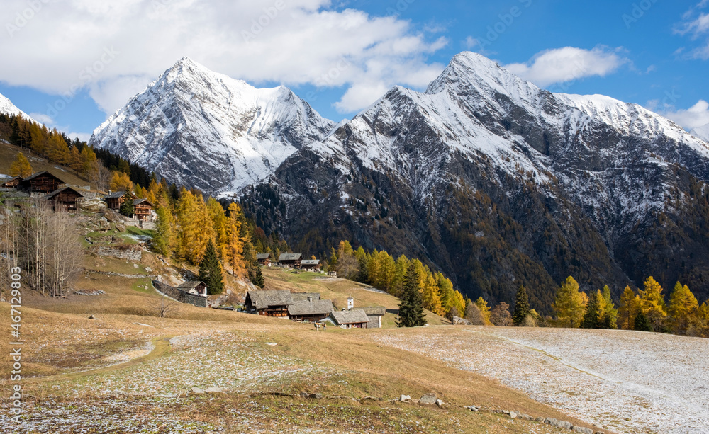 Alpine landscape with traditional wooden houses. Seasonal autumnal scenery in highlands with the first snow of the season. Landscape of the Italian Alps in Piedmont. Otro Valley, Valsesia. 