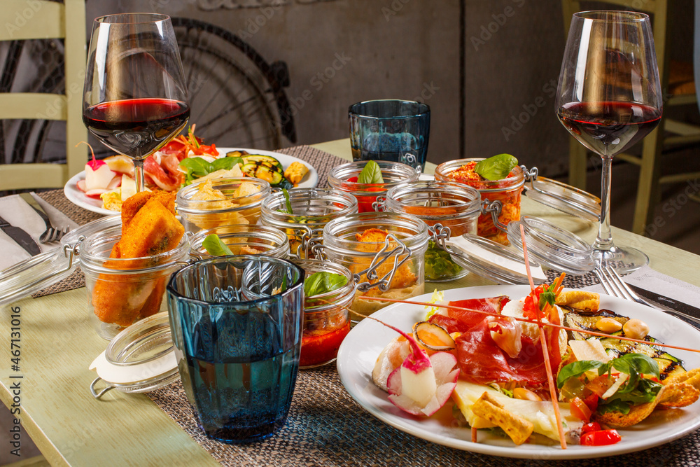 Tavola di un ristorante piena di barattoli con dentro piccoli antipasti misti e con due antipasti misti principali accopagnati da due calici di vino rosso Tavola di un ristorante piena di barattoli con dentro piccoli antipasti misti e con due antipasti misti principali accopagnati da due calici di vino rosso