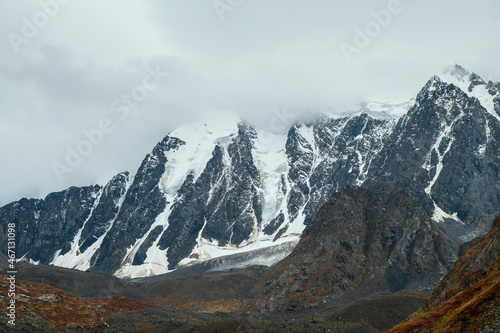 Minimalist atmospheric mountains landscape with big snowy mountain top in low clouds. Awesome minimal scenery with glacier on rocks. High mountain pinnacle with snow in clouds.
