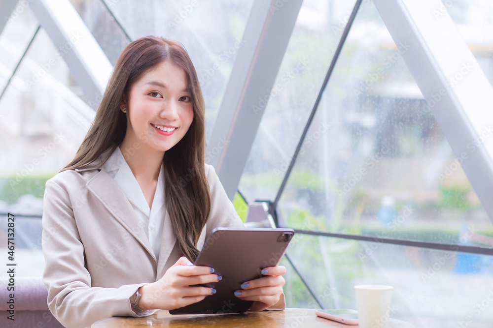 Beautiful young Asian professional business female in a cream-colored suit is looking at the camera while using tablet or notepad in her hands she is sitting happy smile working at coffee shop.
Beautiful young Asian professional business female in a cream-colored suit is looking at the camera while using tablet or notepad in her hands she is sitting happy smile working at coffee shop.