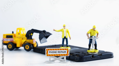Toy men-workers repair a mobile phone or smartphone using a jackhammer and a forklift truck. Smartphone repair and restoration concept. Macro. Selective focusing