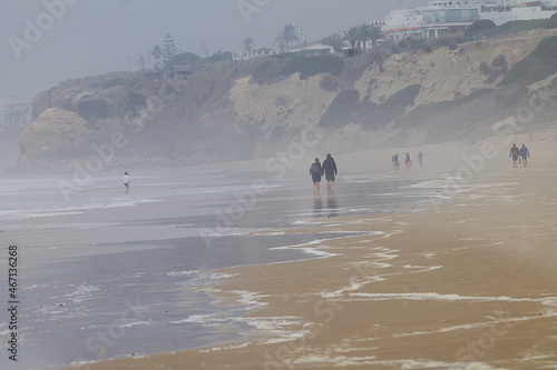 Paisaje personas caminando por la playa en otoño con niebla y mucho viento en Conil de la Frontera, Cádiz