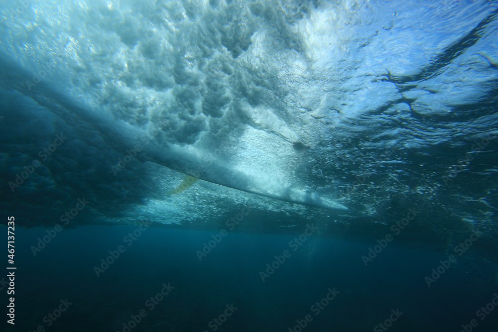 Obraz premium surfer riding a surfboard on a wave photographed from underwater with the sun behind him