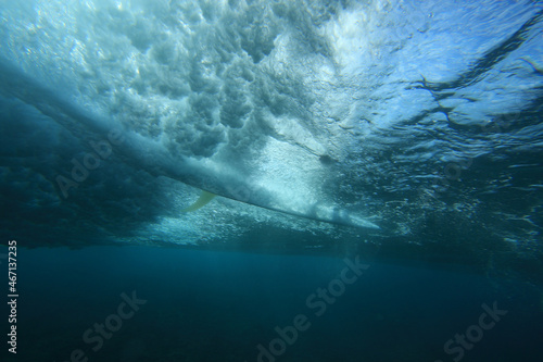 surfer riding a surfboard on a wave photographed from underwater with the sun behind him