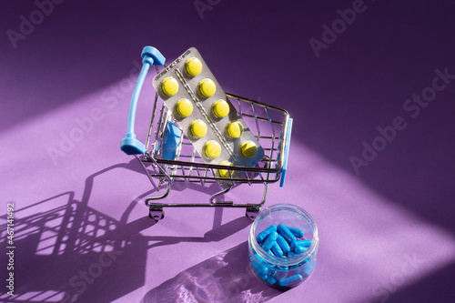 Wallpaper Mural Yellow and blue pills in a small supermarket trolley. Delivery of pills from pharmacies. Purple background.  Torontodigital.ca