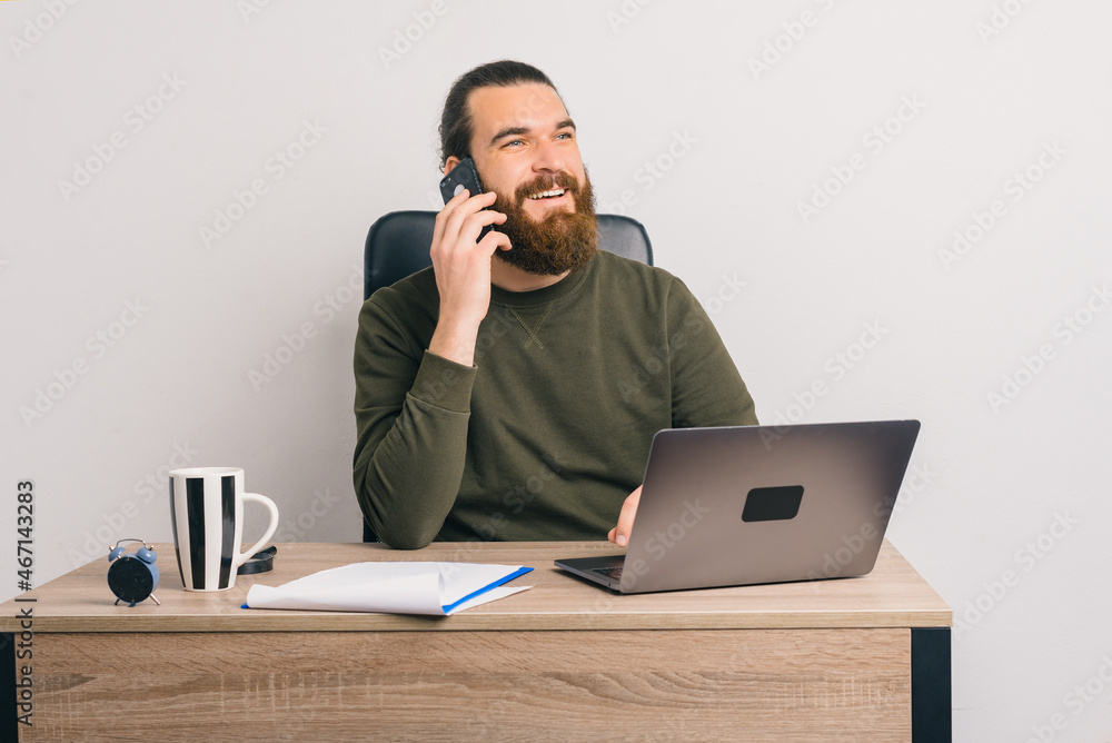 Friendly young bearded man is talking on the phone in the office. Friendly young bearded man is talking on the phone in the office.