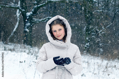 Young girl in the winter forest during a snowfall. Portrait of a young happy girl in the winter forest