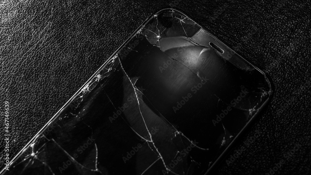 Broken glass screen smartphone on a black textured background. Cracked glass on a screen. Crash phone, fractured, smartphone repair, regret concept. Selective focus, close up