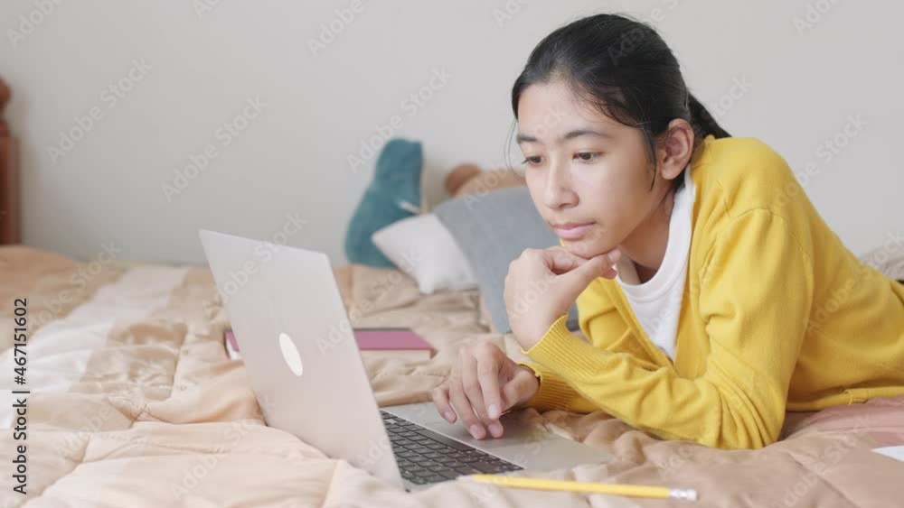 Asian woman using a laptop while lying on bed at home morning, learning