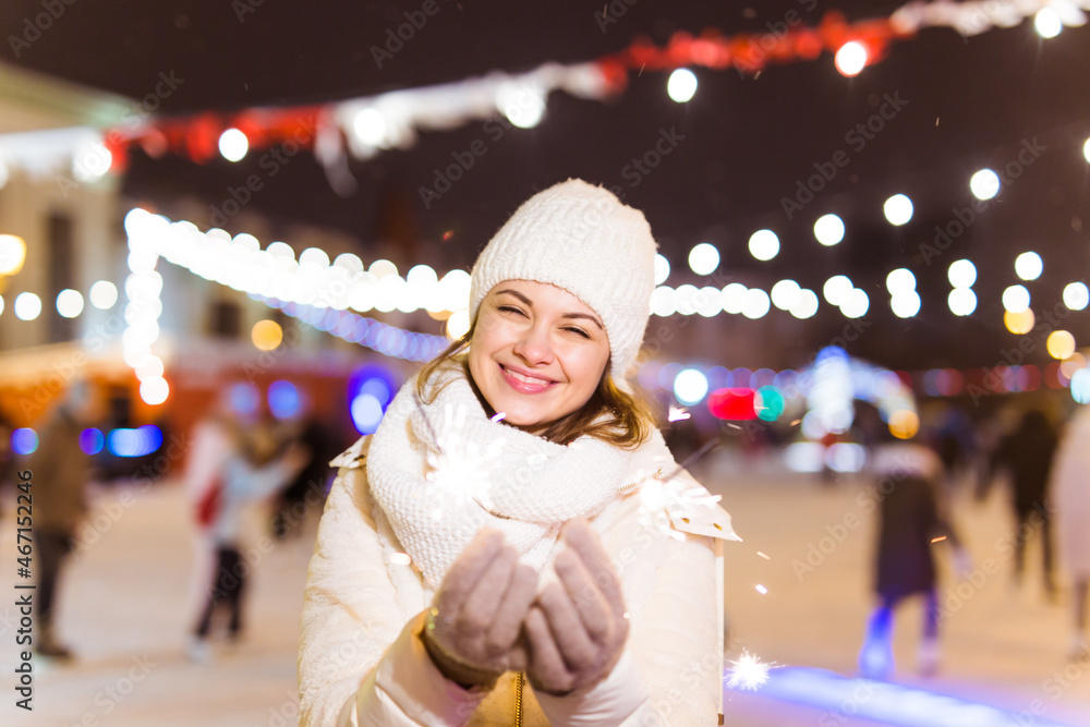 Girl holding a sparkler in her hand. Outdoor winter city background, snow, snowflakes. Girl holding a sparkler in her hand. Outdoor winter city background, snow, snowflakes.