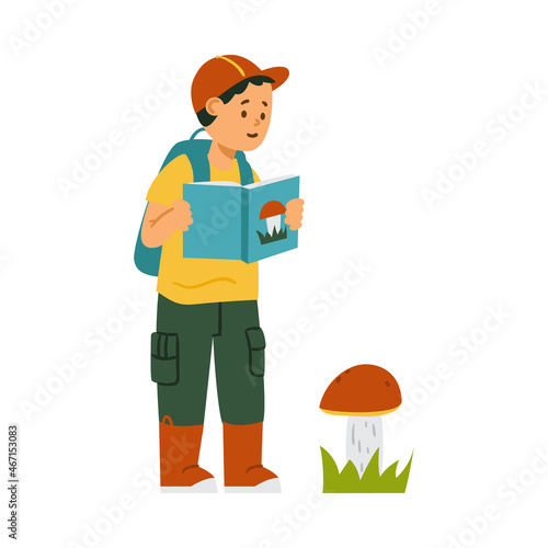 Hiking boy with backpack and in rubber boots watch big mushroom and read about fungi in his education book.