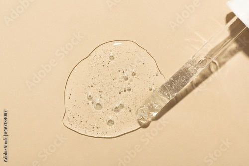 Obraz na płótnie Spilled clear serum with bubbles and glass pipette on beige surface close upper view. Skincare and dermatological procedures w salonie