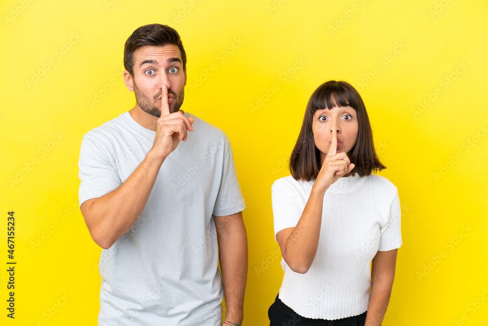 Young couple isolated on yellow background showing a sign of silence gesture putting finger in mouth Young couple isolated on yellow background showing a sign of silence gesture putting finger in mouth