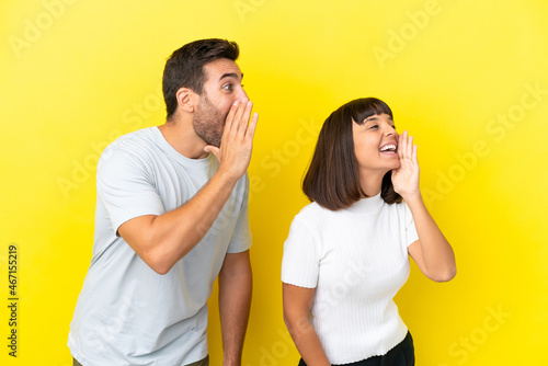 Young couple isolated on yellow background shouting with mouth wide open to the lateral
