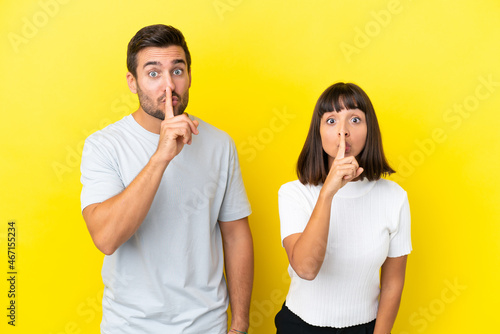 Young couple isolated on yellow background showing a sign of silence gesture putting finger in mouth