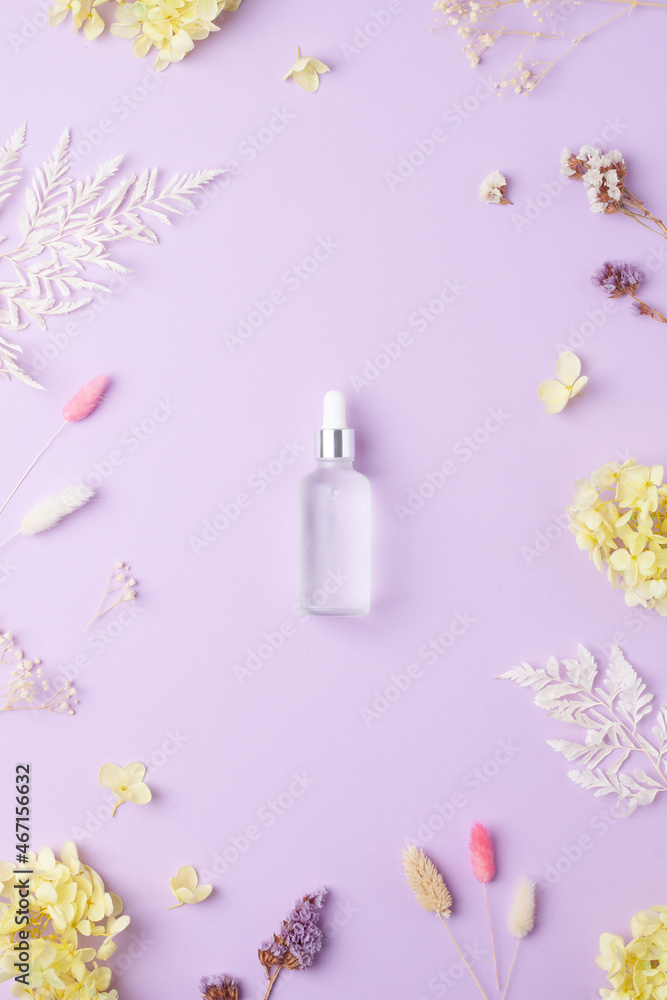 Cosmetic bottle with flowers on rose background. Flat lay
