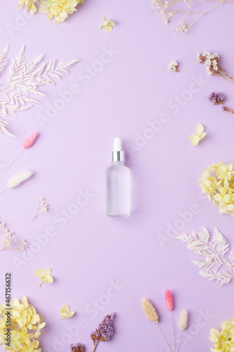 Cosmetic bottle with flowers on rose background. Flat lay