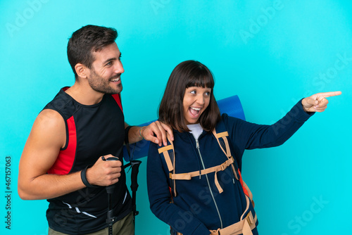 Young mountaineer couple with a big backpack isolated on blue background presenting an idea while looking smiling towards