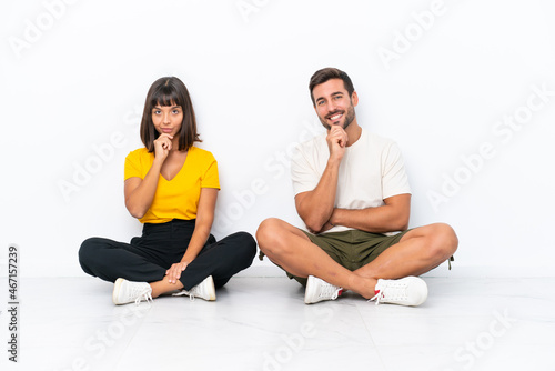Young couple sitting on the floor isolated on white background smiling and looking to the front with confident face