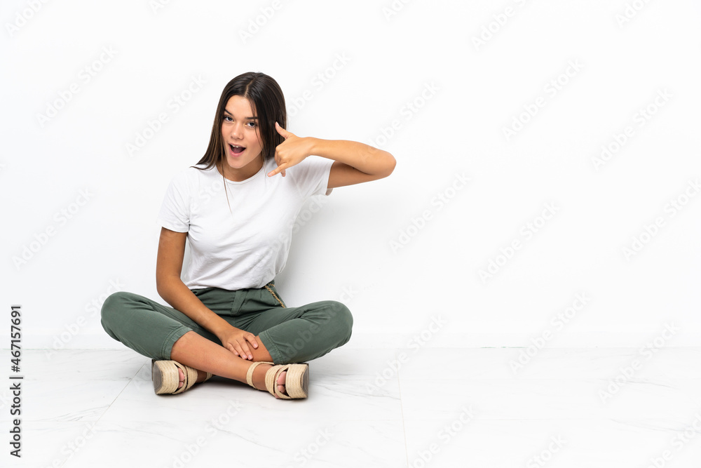 Teenager girl sitting on the floor making phone gesture. Call me back sign Teenager girl sitting on the floor making phone gesture. Call me back sign