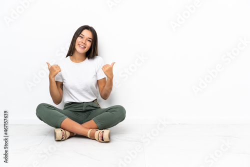 Teenager girl sitting on the floor with thumbs up gesture and smiling