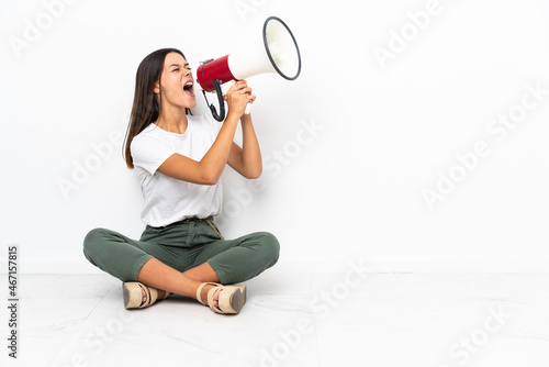 Teenager girl sitting on the floor shouting through a megaphone