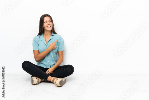 Free Download Teenager girl sitting on the floor pointing to the side to present a product - GFXLoad