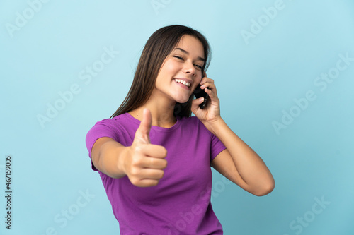 Teenager girl isolated on pink background keeping a conversation with the mobile while doing thumbs up