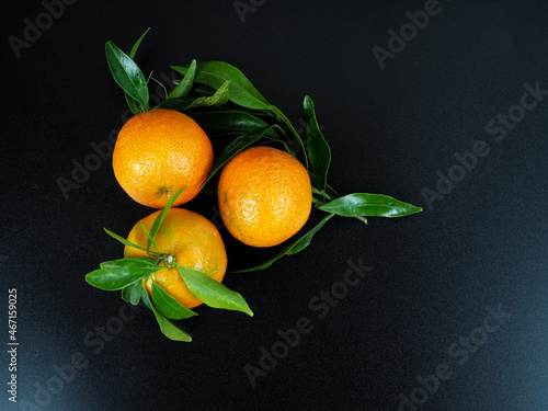 Fresh tangerines with green leaves on a black background. Top view